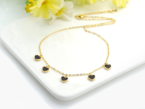 Gold-tone black heart charm necklace beside pale flowers on a white tray