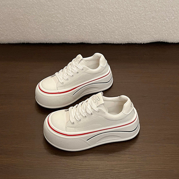 White lace-up platform sneakers with thin red stripe and dark side trim on a brown floor
