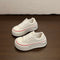 White lace-up platform sneakers with thin red stripe and dark side trim on a brown floor