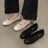 Beige perforated bow ballet flats worn beside a black pair