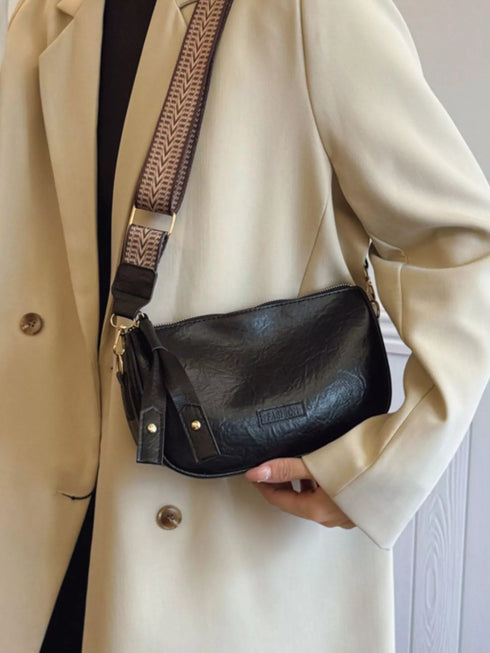 Side view of black crossbody bag worn with a cream coat