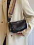 Side view of black crossbody bag worn with a cream coat