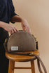 Hopper bag on a wooden stool with hands holding the opening