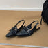 Pointed-toe studded slingbacks reflected in a mirror on a woven rug