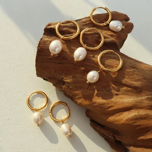 Several gold-plated pearl hoop earrings arranged on wood with a pair on white