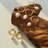 Several gold-plated pearl hoop earrings arranged on wood with a pair on white