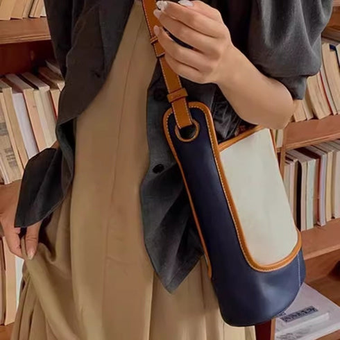 Side view of beige canvas and navy shoulder bag with brown adjustable strap