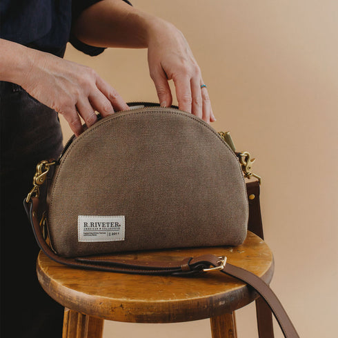 Hopper bag on a stool with the wearer holding the zipper opening
