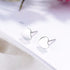 Pair of polished silver heart stud earrings angled on a white card