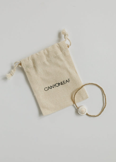 Single CanyonLeaf conch-shell stretch bracelet beside a branded drawstring pouch
