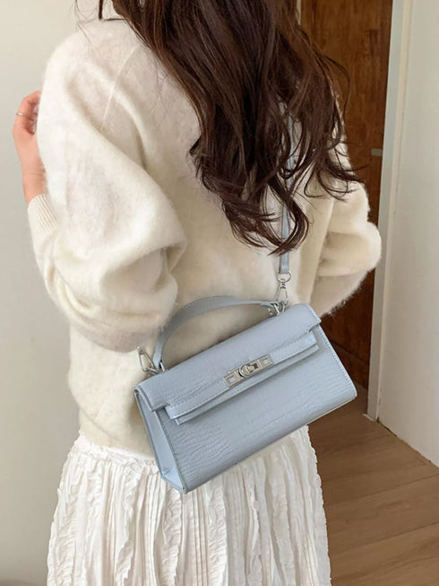 Blue croc-embossed bag worn over the shoulder, showing the back panel and top handle