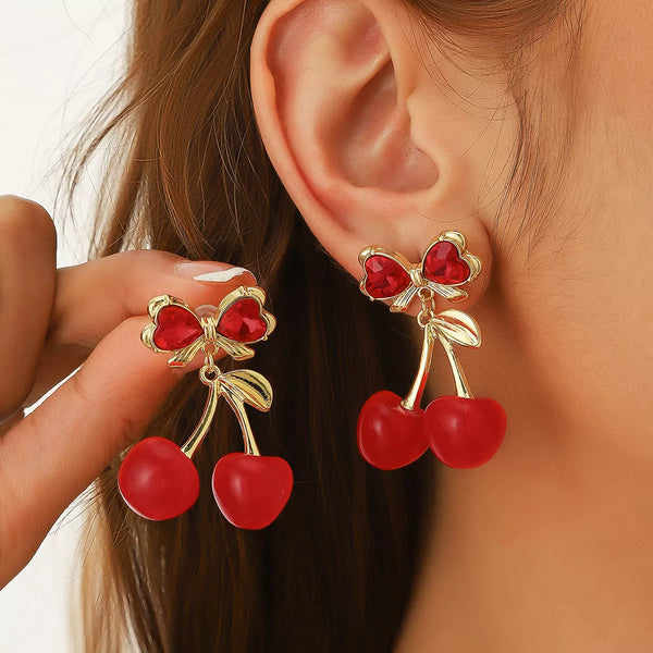 Red cherry drop earring with red bow detail worn on an ear