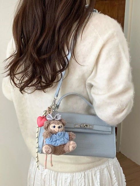 Blue faux leather crossbody bag shown from the side on a model with a cream sweater