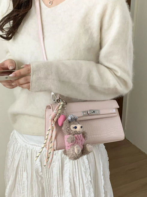 Pink croc-embossed crossbody bag worn at the hip with a pink teddy bear charm
