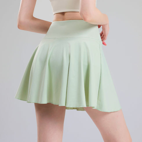 Green tennis skort modeled from the side, showing high waistband and flowing pleats