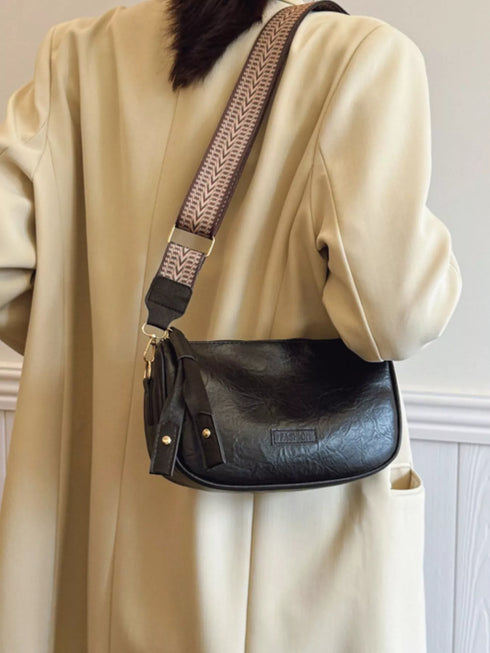 Black crossbody bag worn across a cream coat