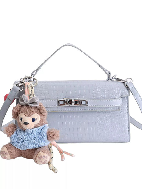 Blue croc-embossed faux leather bag with top handle, crossbody strap and teddy bear charm on white