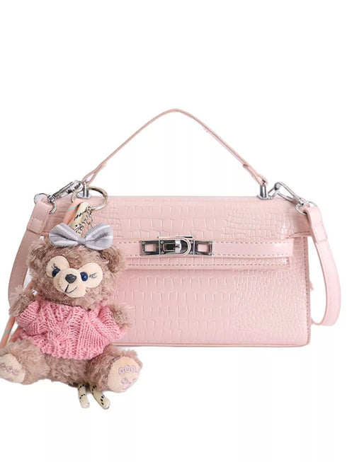 Pink croc-embossed faux leather bag with top handle, strap and teddy bear charm on white