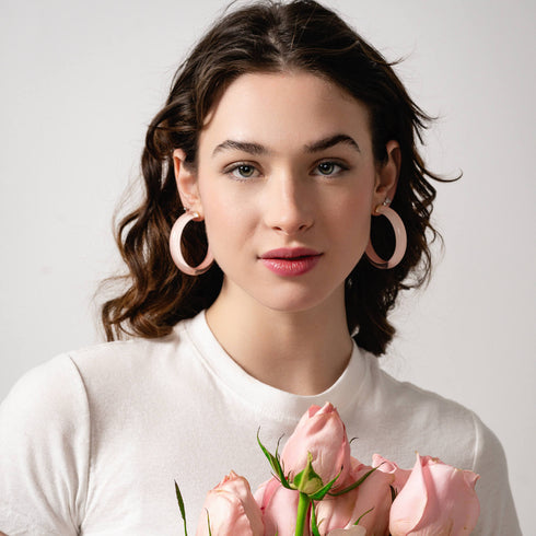 Model wearing pale pink Lucite hoop earrings with a white top