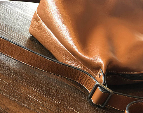 Detail of brown leather surface, stitching and strap hardware