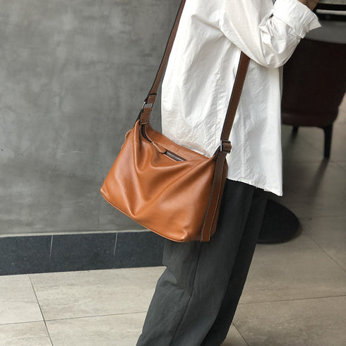 Model carrying warm brown leather crossbody with a white blouse