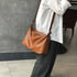 Model carrying warm brown leather crossbody with a white blouse