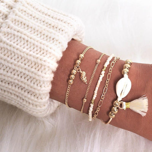 Gold-tone bracelet stack with shell-shaped charm, pale tassel and leaf detail