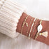 Gold-tone bracelet stack with shell-shaped charm, pale tassel and leaf detail