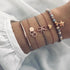 Rose-tone bracelet stack with gray beads, bow and linked geometric charms