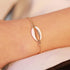 Close-up of a single gold-tone bracelet with a pink shell-shaped centerpiece