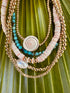 Close-up of conch-shell gold-filled bracelet among other beaded strands on a green leaf