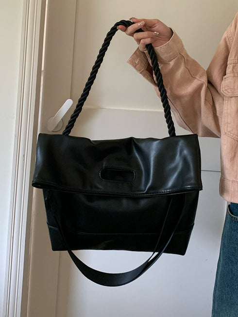 Black hobo bag held by its braided shoulder strap