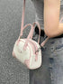 Mini bowling bag worn crossbody, showing pink strap and cream front