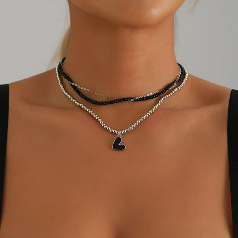 Black beaded layers with a black heart pendant, modeled against a black top