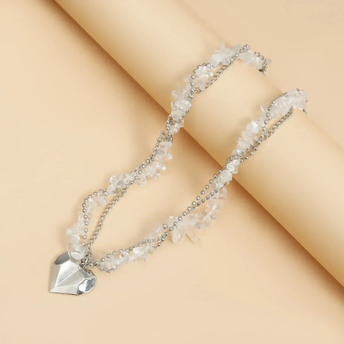 Pale bead necklace with large heart pendant arranged on beige