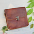 Close front view of brown leather flap bag and brass clasp