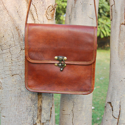 Brown leather crossbody hanging from a tree with brass clasp visible