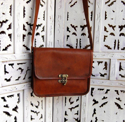 Front of vintage-brown leather crossbody hanging against a decorative screen