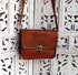 Front of vintage-brown leather crossbody hanging against a decorative screen