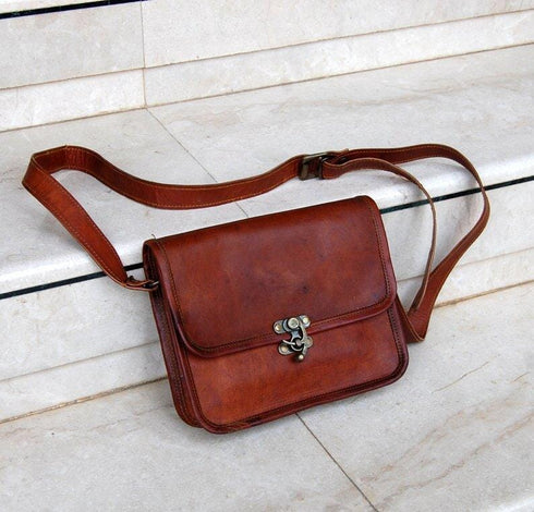 Brown leather crossbody bag laid on stone with adjustable strap