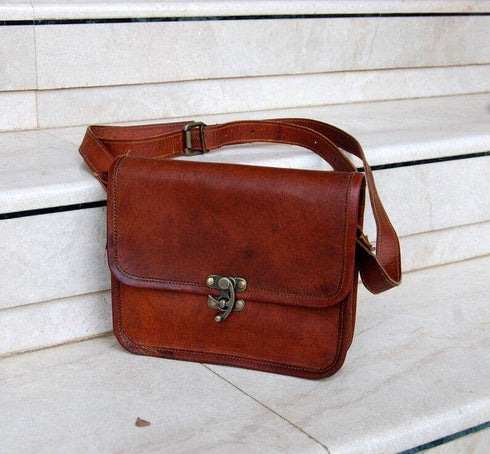 Brown leather shoulder bag with adjustable strap on a stone bench