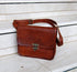 Brown leather shoulder bag with adjustable strap on a stone bench