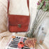 Brown leather crossbody styled beside magazines and flowers