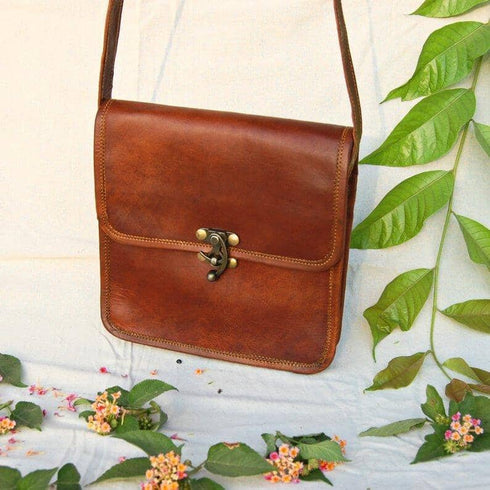 Brown leather flap bag hanging above flowers with strap extended