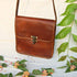 Brown leather flap bag hanging above flowers with strap extended