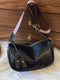 Black retro faux leather crossbody bag with wide patterned strap against wood