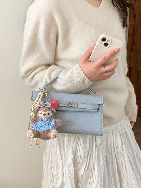 Blue croc-embossed crossbody bag held by its top handle with a teddy bear charm