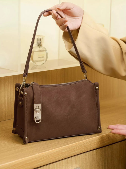 Brown Buckle-Detail Crossbody Bag: Brown bag standing on a table with strap raised