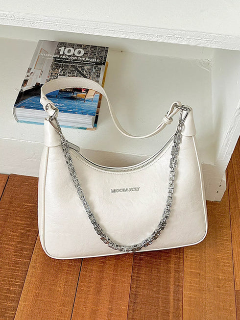 Chain-Detail Shoulder Bag: White chain-detail bag displayed on wooden table