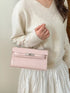 Pink croc-embossed faux leather bag carried by its top handle against a cream outfit